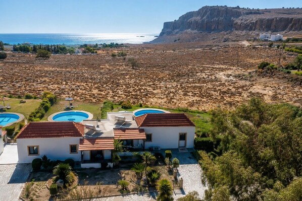 A resort with a pool area, a building with a red-tiled roof, and a view of the sea and cliffs. - Villa Sandpiper - Two Bedroom Villa, Sleeps 4 (Lindos)