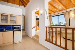 Cuina moderna amb armaris de fusta, microones i rentavaixelles. Hi ha un balcó amb barana de fusta i vista a palmeres.