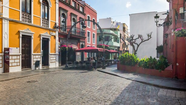 Una calle empedrada bordeada de edificios coloridos, con mesas al aire libre y jardineras.