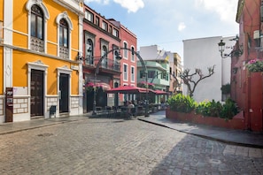 A cobblestone street lined with colorful buildings, outdoor seating, and a tree planter. - Vacation Home 'Gáldar-centro' with Private Terrace, Balcony, and Wi-Fi (Gáldar)