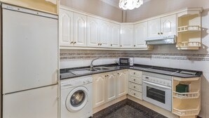 Una cocina con muebles blancos, lavadora, microondas y estufa.