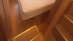 Een klein, gelijkvloers houten blokhutje met een bed, een raam en inbouwkastjes.