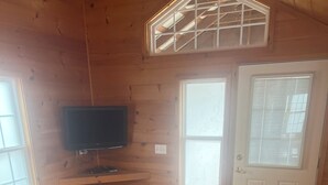 Een gezellig houten interieur met een grijze bank, een televisie aan de wand en een raam met zonwering.