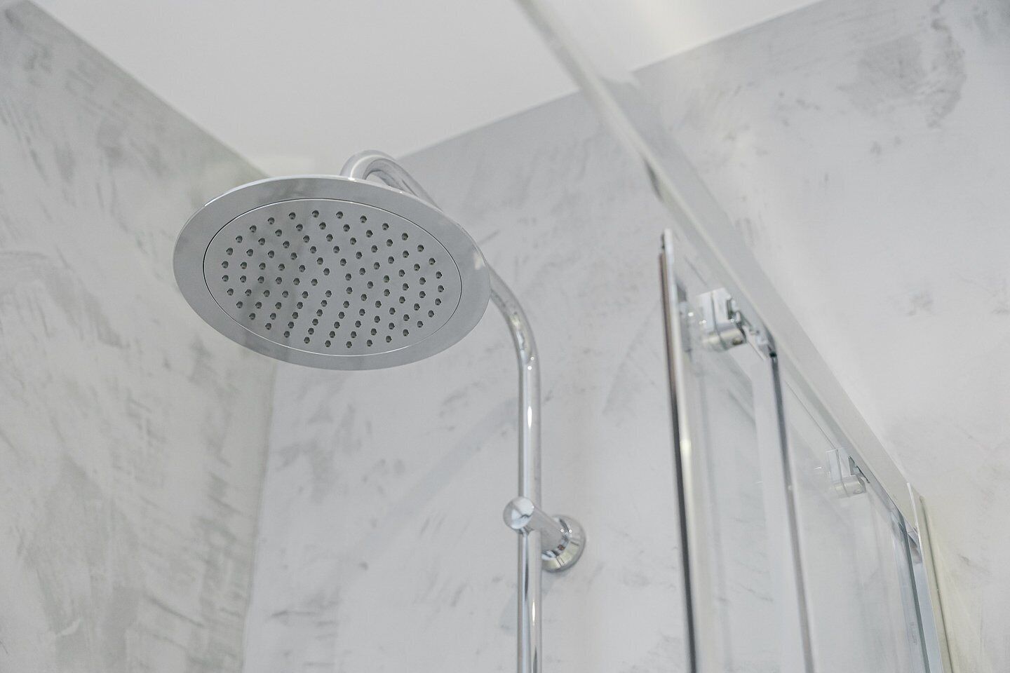 Un pommeau de douche de forme circulaire et perforée, installé dans une salle de bain aux murs recouverts de marbre.