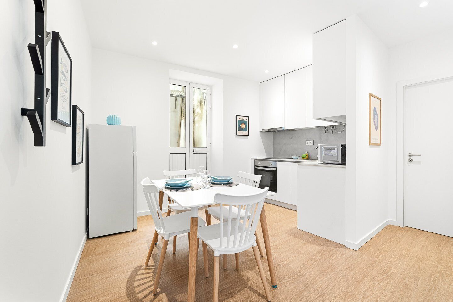 A modern kitchen with white cabinetry, a dining table with chairs, and a refrigerator.