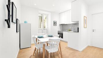 A modern kitchen with white cabinetry, a dining table with chairs, and a refrigerator.