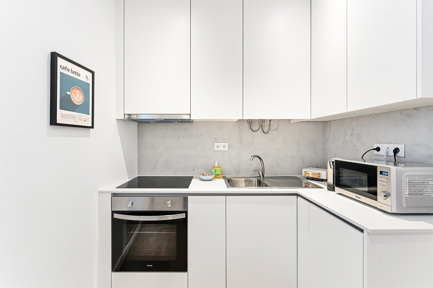 A modern kitchen with white cabinets, a built-in oven, a microwave, and a sink.