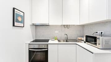 A modern kitchen with white cabinets, a built-in oven, a microwave, and a sink.