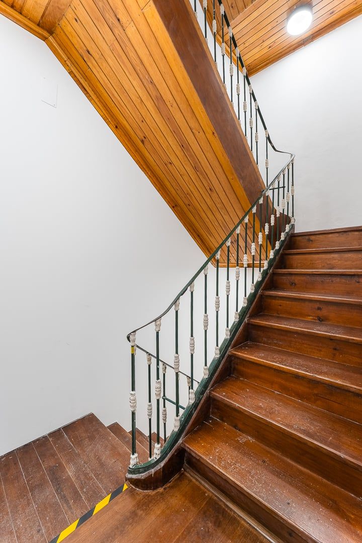 Un escalier en bois à la forme incurvée, doté de rampes en métal et adossé à un mur blanc.