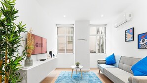 A modern living room with a grey sofa, blue cushions, a blue rug, a small round table, a TV, and a plant. - GuestReady - The Olives - Blue (Coimbra)