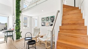 En modern inredning med en trätrappa, en grön vertikal trädgård och en sittgrupp med två stolar och ett litet bord.