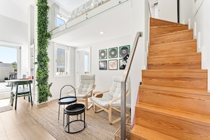 A modern interior with a wooden staircase, a green vertical garden, and a seating area with two chairs and a small table. - GuestReady - Cosy stay in Bonfim (Porto)