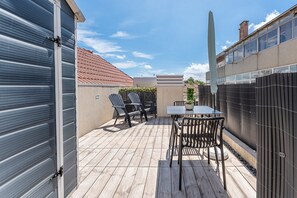 En terrasse med et bord, stole, en potteplante og en høj obelisk.