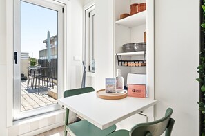 A room with a white table, green chairs, a window with a view of buildings, a shelf with kitchenware, and a 'Guest Ready' sign. - GuestReady - Cosy stay in Bonfim (Porto)