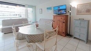 En matplats med ett runt bord, stolar, ett skåp och en tv som hänger på väggen.