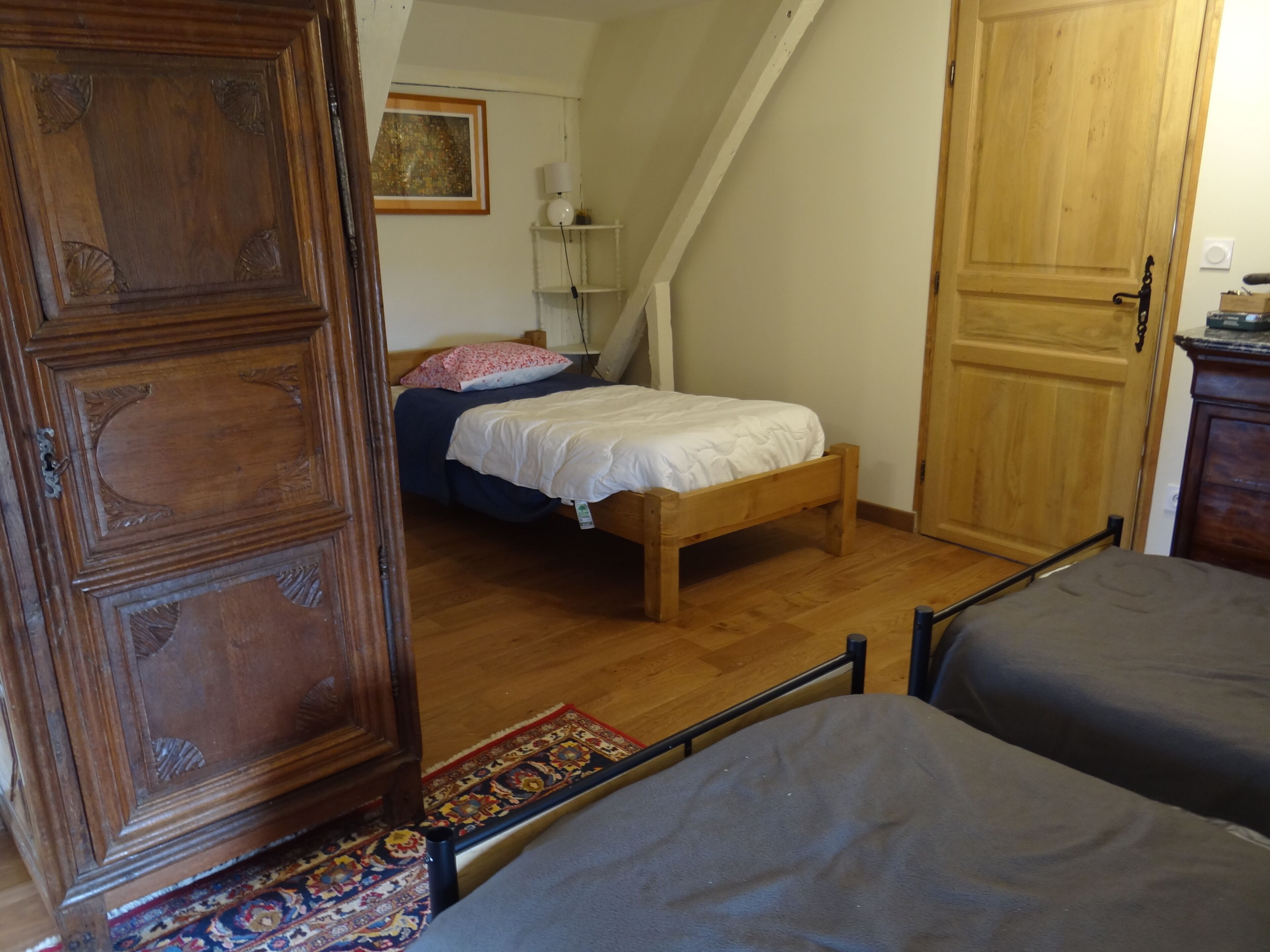 Un dormitorio con un armario de madera, una cama con edredón blanco, piso de madera y una alfombra pequeña.