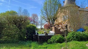 A stone building with a conical roof, surrounded by lush greenery and flowering plants. - La Provosterie (Ahuillé)