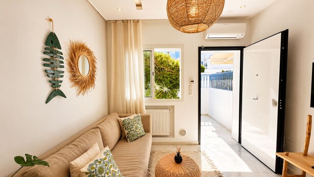 A modern living room with a beige sofa, decorative wall art, a woven pendant light, and a view through a glass door. - Cocon Vert Cozy Apartment in Sidi Bou Saïd (Sidi Bou Said)