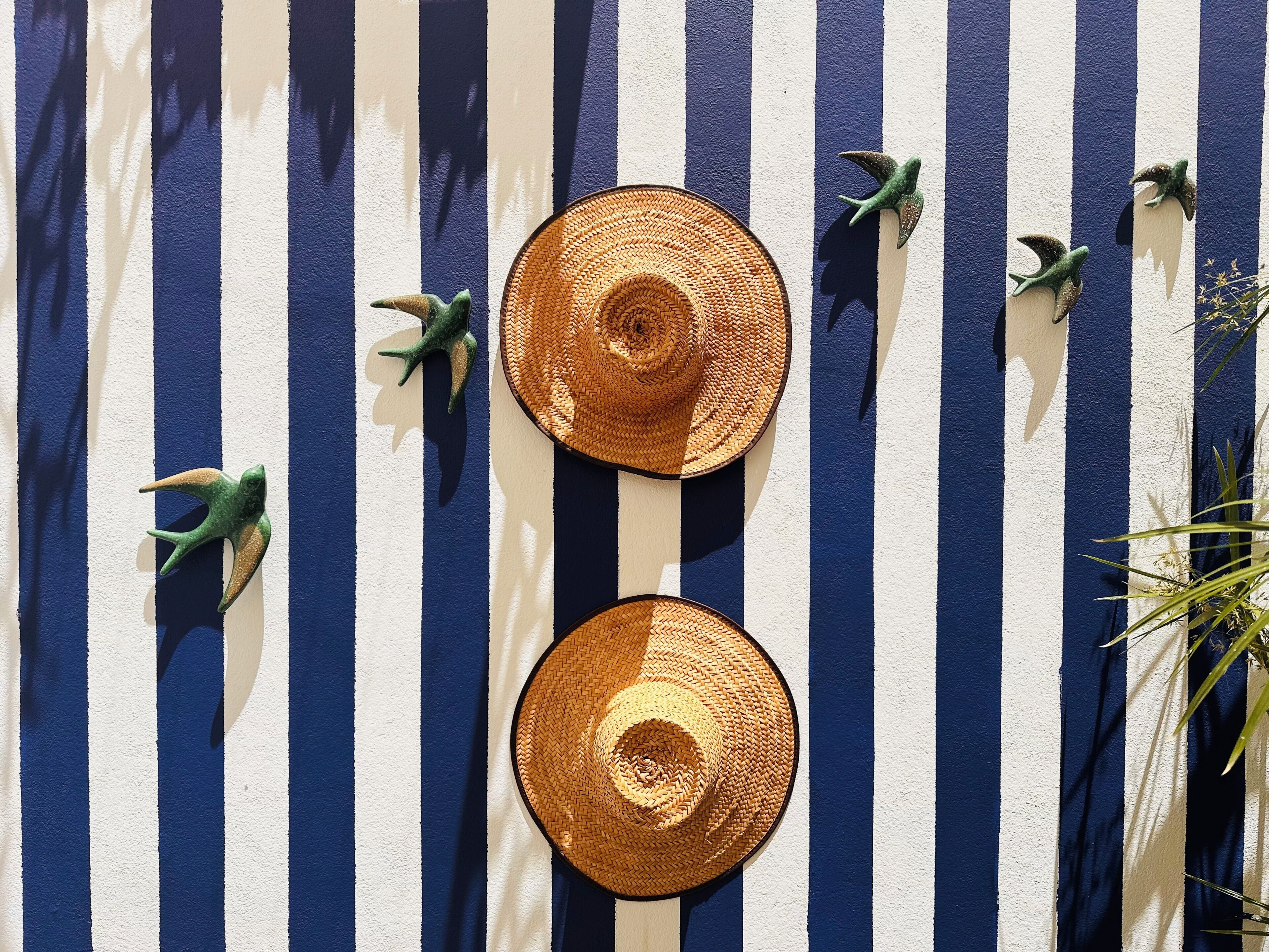 Two straw hats on a striped surface with decorative bird figures.