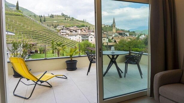 A balcony with a view of a town and vineyards, a yellow chair, and a table with chairs. - Zilli Studio Apartments (Termeno Sulla Strada del Vino)