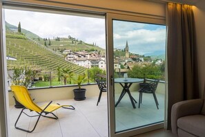 A balcony with a view of a town and vineyards, a yellow chair, and a table with chairs. - Zilli Studio Apartments (Termeno Sulla Strada del Vino)