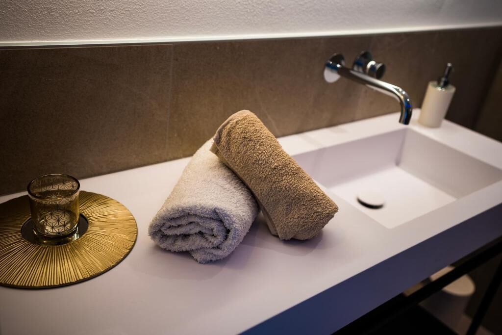 A bathroom sink with two towels, a glass, and a soap dispenser.
