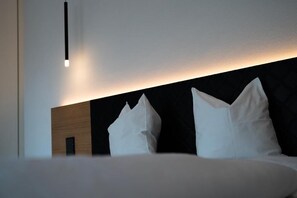 Ett modernt hotellrum med en sänggavel i trä, vita kuddar och ett nattduksbord.