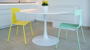 A modern kitchen with white cabinetry, a round white table, and two chairs, one yellow and one green. - Zilli Studio Apartments (Termeno Sulla Strada del Vino)