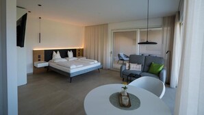 A modern hotel room with a bed, a sofa, a dining table, and a TV. - Zilli Studio Apartments (Termeno Sulla Strada del Vino)