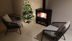 A cozy living area with a fireplace, two black wicker chairs, a small Christmas tree, and a white table. - Zilli Studio Apartments (Termeno Sulla Strada del Vino)