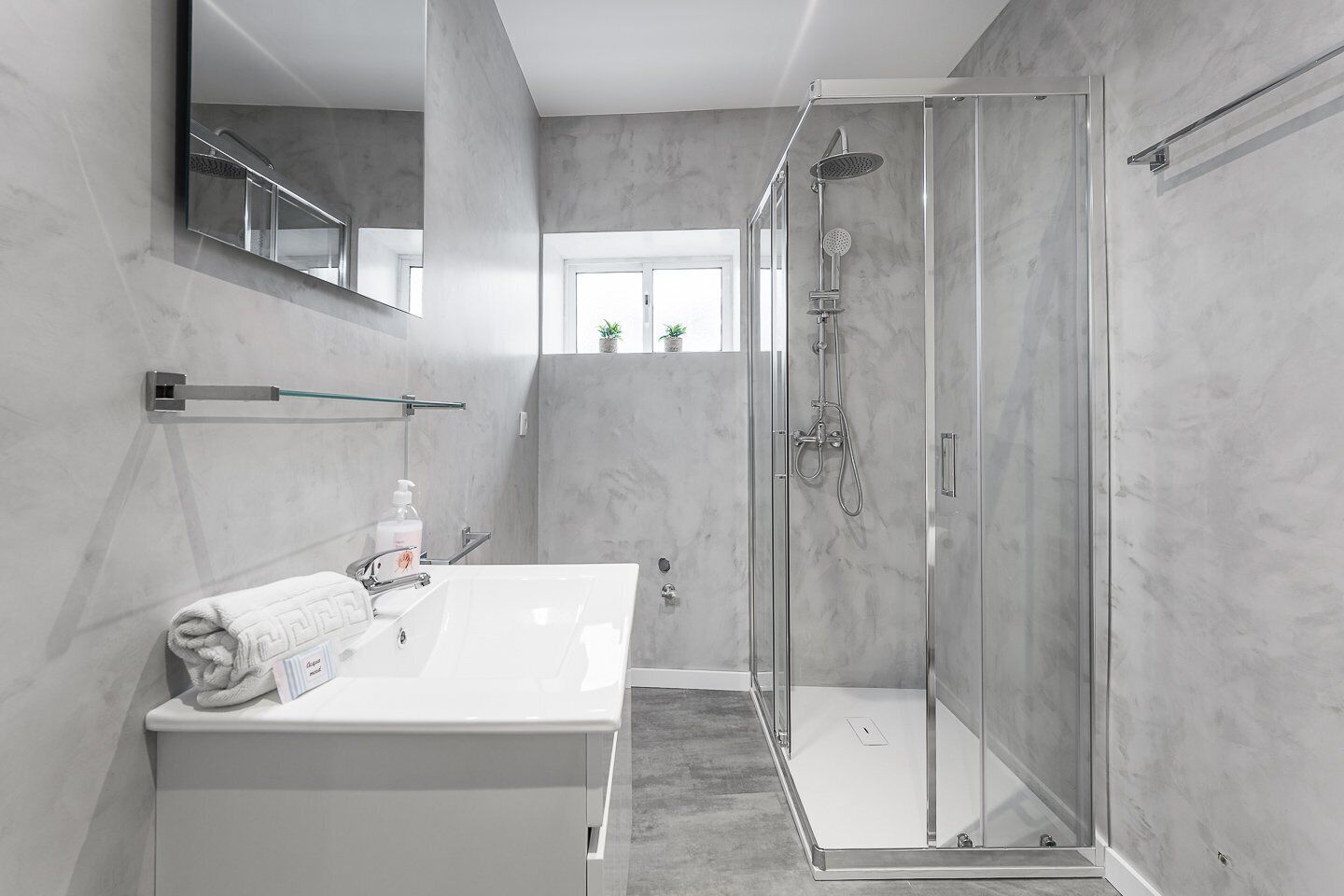 Un baño moderno con ducha envuelta en vidrio, un lavabo blanco y un espejo grande.