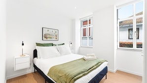 Un dormitorio con cama, mesita de noche y ventana, con vistas al exterior.