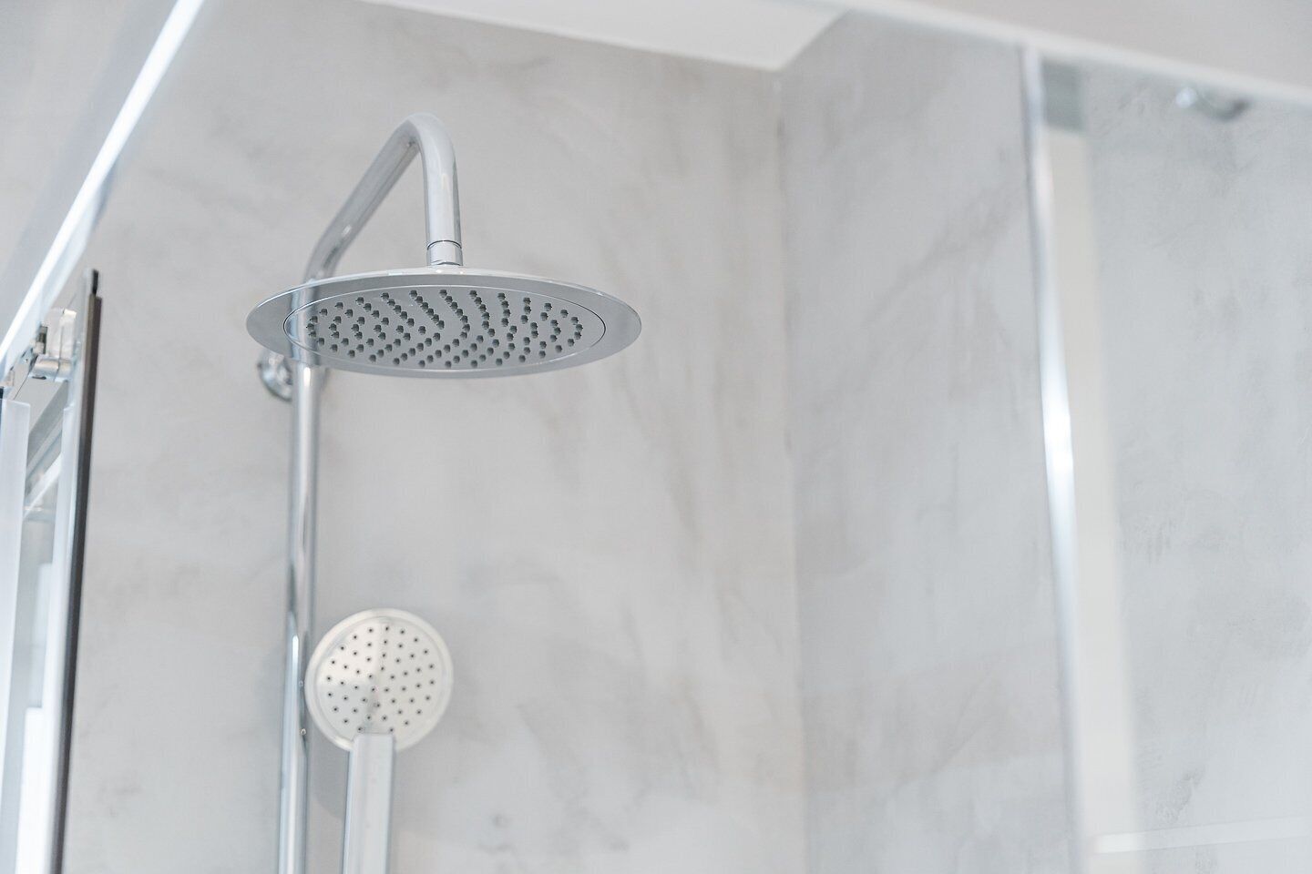 Une douche équipée d’un pommeau de douche à effet pluie et d’un pommeau de douche portatif, dans une salle de bain aux murs recouverts de marbre.
