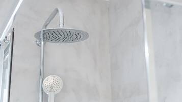 Une douche équipée d’un pommeau de douche à effet pluie et d’un pommeau de douche portatif, dans une salle de bain aux murs recouverts de marbre.