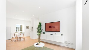 Una sala de estar moderna con un televisor de pantalla plana, un comedor con mesa y sillas, una planta en maceta y una alfombra verde.