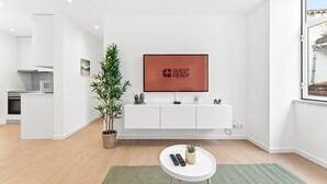 Habitación de hotel moderna con diseño minimalista, que incluye una consola blanca, un televisor de pantalla plana, una pequeña planta en maceta y un control remoto sobre una mesita auxiliar blanca.