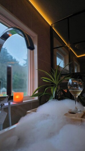 Ein Badezimmer mit modernem Wasserhahn, einer Kerze, einem Glas Weißwein und einem Blumentopf.