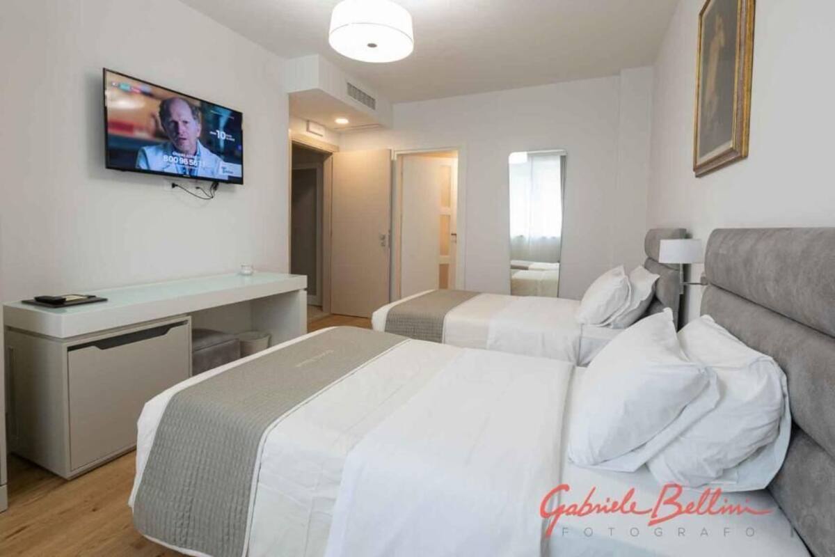 A hotel room with two beds, a desk, a television, and a painting on the wall.