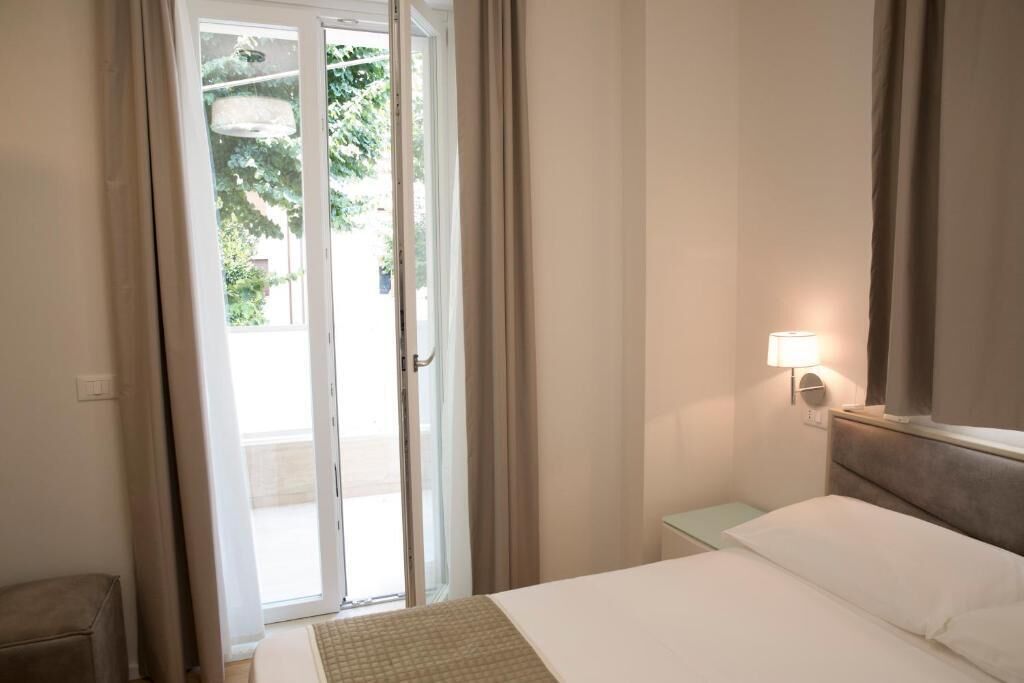 A hotel room with a bed, a nightstand, a lamp, and a sliding glass door leading to an outdoor area.