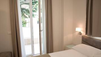 A hotel room with a bed, a nightstand, a lamp, and a sliding glass door leading to an outdoor area.