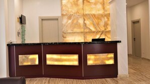 Una recepción con pared de mármol, un televisor y una puerta al fondo.