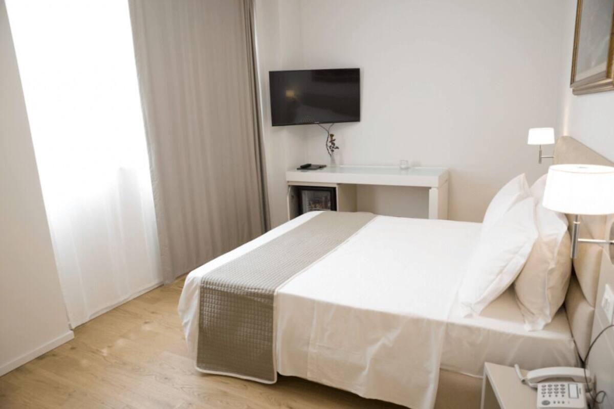 A hotel room with a bed, a bedside table, a TV mounted on the wall, and a phone on the table.
