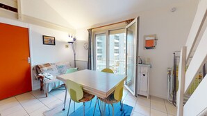 A compact living space with a dining table, chairs, a sofa, and a balcony with a view of the building. - Ciel de Bora - Panoramic Ocean View & Parking (Saint-Hilaire-de-Riez)