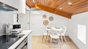 Una cocina moderna con techo de madera, armarios blancos y un comedor con sillas y mesa blancos.