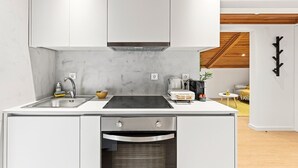 Una cocina moderna con armarios blancos, un lavamanos de acero inoxidable, una placa de inducción negra y un horno empotrado.