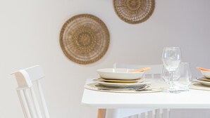 Una mesa de comedor con platos blancos, un vaso y un bol. Encima de la mesa hay tres decoraciones de pared tejidas.
