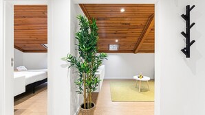 Una habitación con cama, una planta en maceta, una mesita con una vela y un perchero.