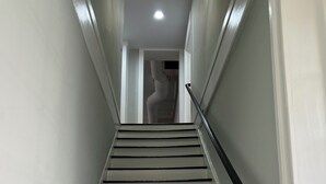 Una scala con pareti bianche e corrimano neri che conduce a una stanza con una luce a soffitto.