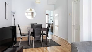 A modern living room with a flat-screen TV, a dining table with chairs, a round mirror, and a grey sofa. - Traditional Belfast Home, Walking Distance to City & Titanic Heritage (Belfast)