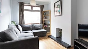 A modern living room with a grey sofa, a bookshelf, a fireplace, and a TV. - Traditional Belfast Home, Walking Distance to City & Titanic Heritage (Belfast)
